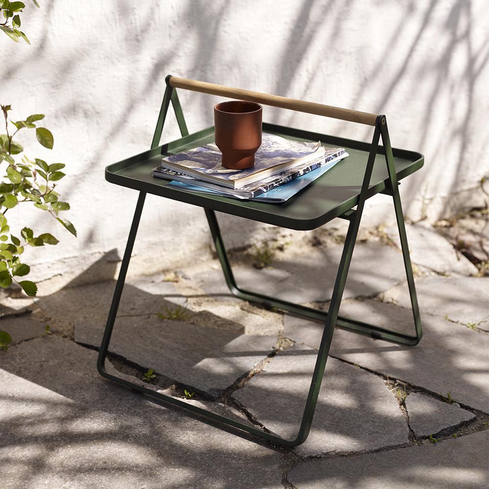 A small green outdoor table stacked with magazines and a ceramic cup