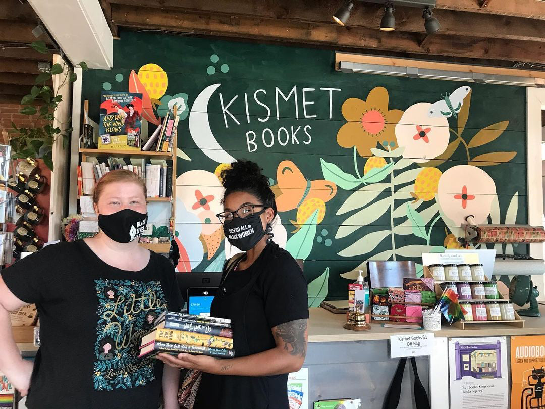 Dominique Lenaye visits another bookstore owner in her store. A wall mural behind them reads "Kismet Books"
