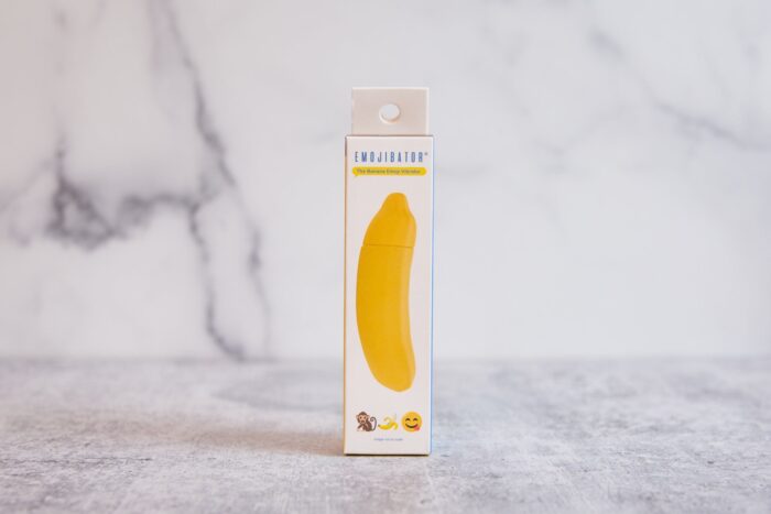 A boxed sex toy sits on a marbled surface. The label reads "Emojibator" and features a banana