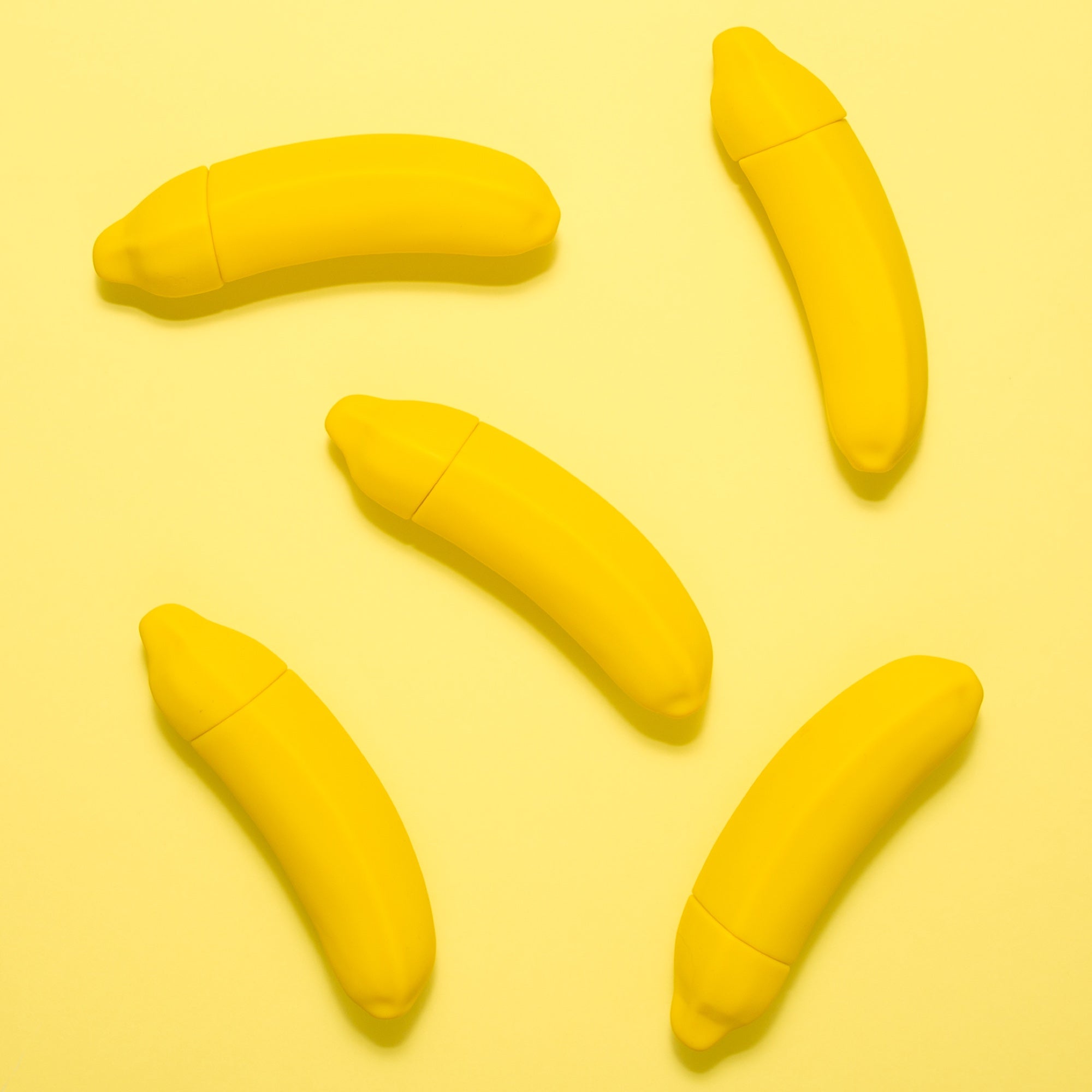 Five banana vibrators lay on a yellow background
