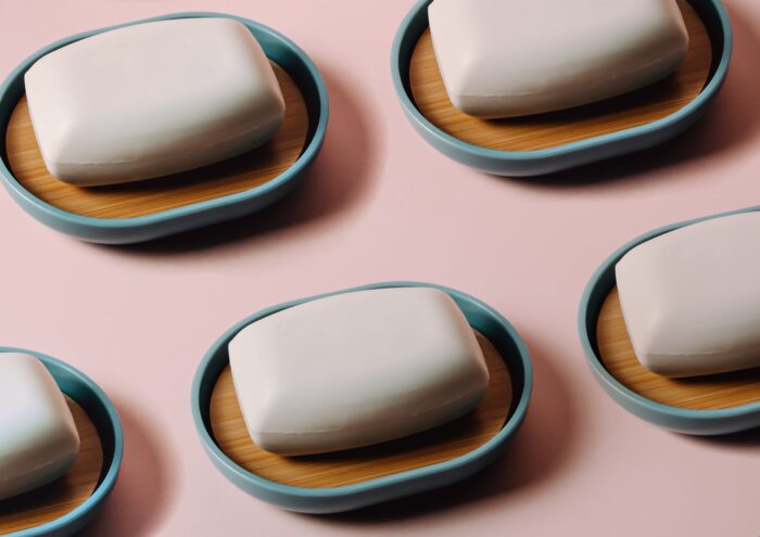 Several bars of soap are arranged on soap dishes on a pink background