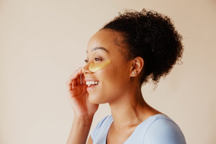 A smiling woman uses an eye mask skincare product