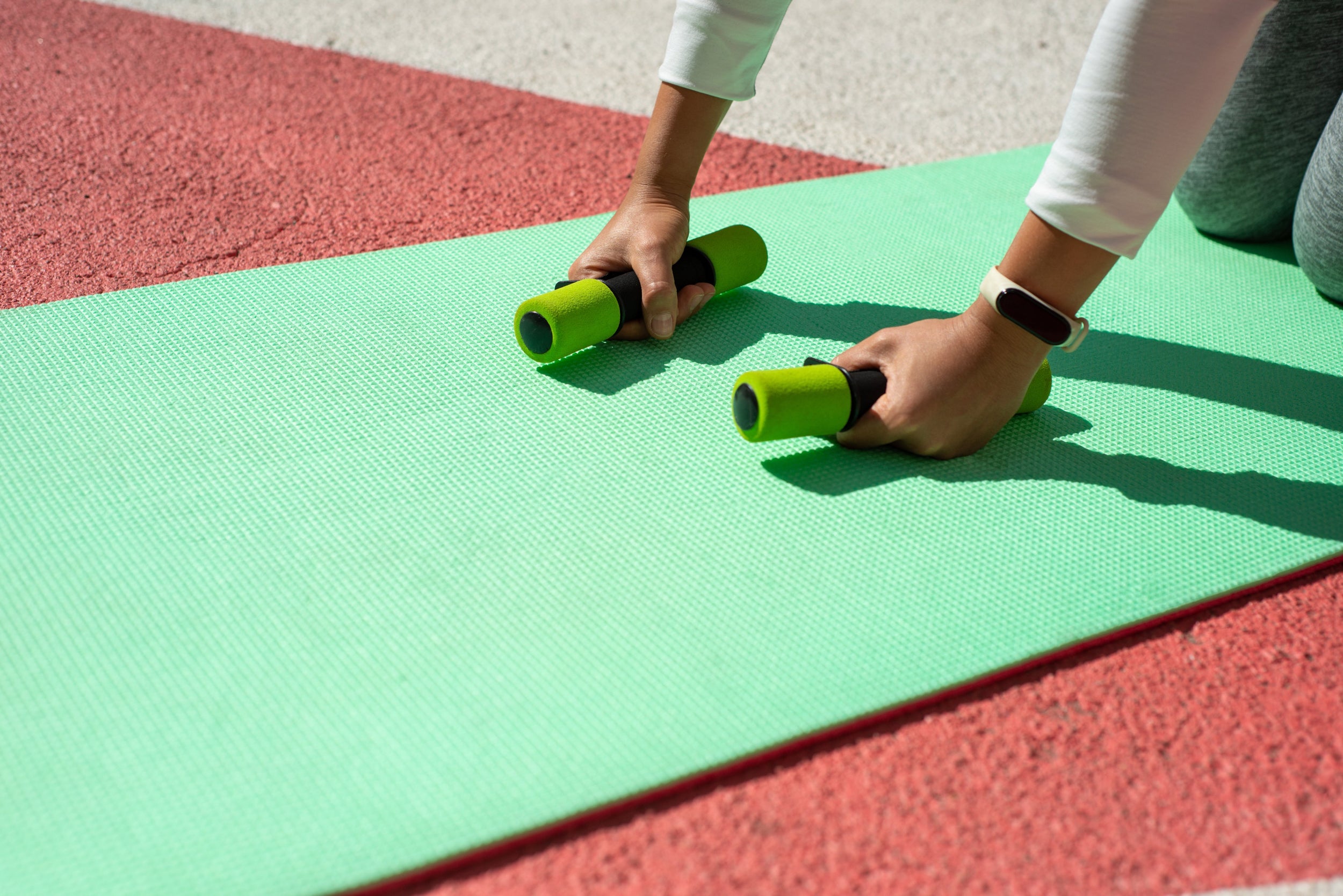 Two hands hold fitness weights on a green yoga mat