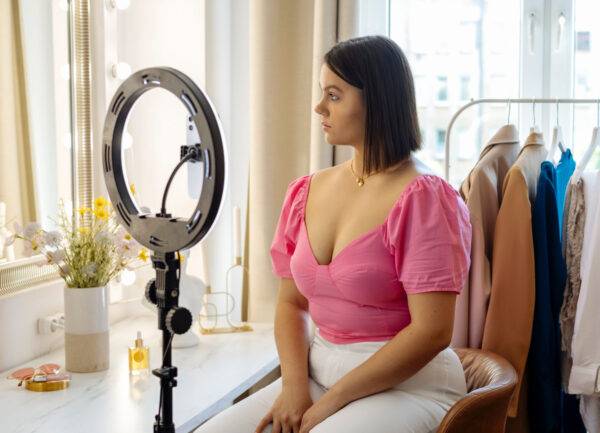 Woman preparing to record content in a room with clothes and a ring light.