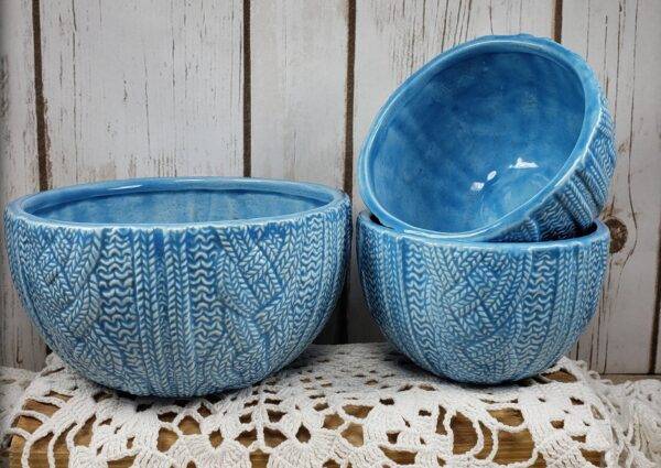 Pottery bowls in blue glaze are stacked on a lace tablecloth on a wooden table