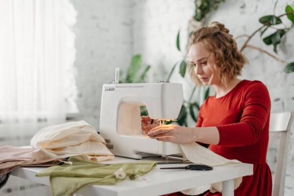 Woman sewing with a machine at a table with fabric.