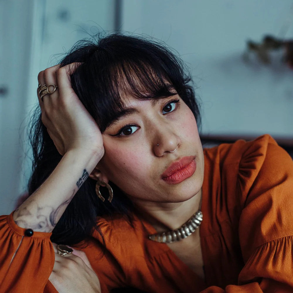 A woman leans her head on her hand while modeling jewelry