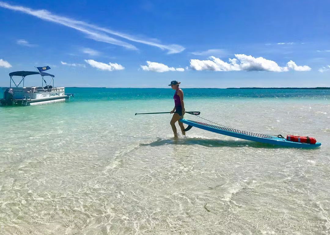 A person drags a paddleboard across the beach