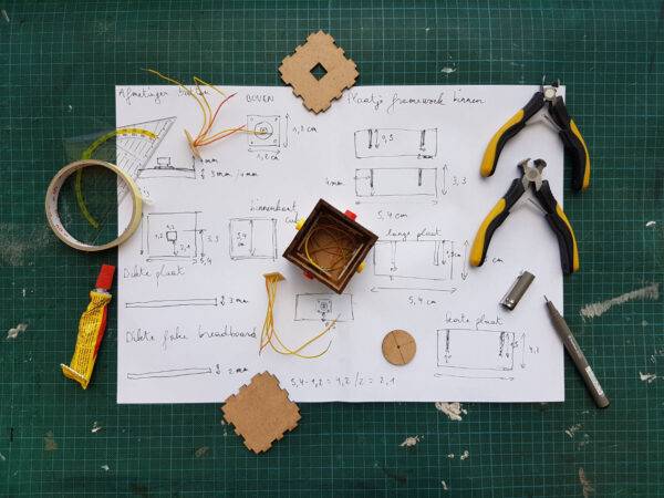 Flatlay of sketched product blueprints with drafting tools on a green grid work surface