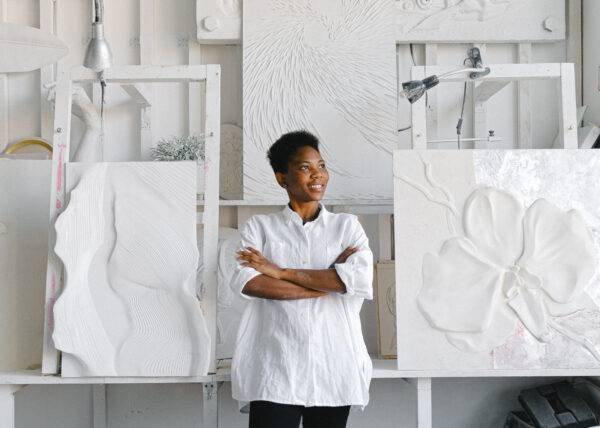 An artist stands in her studio in from of white textural art