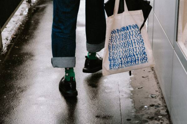 Person walking with a tote bag on a wet street.