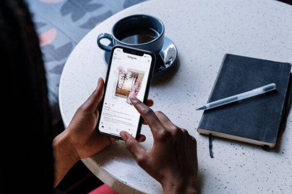 Person using a smartphone while sitting at a table with a coffee and notebook.