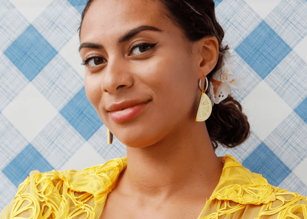 A woman wearing a yellow dress models earrings shaped like lemon wedges