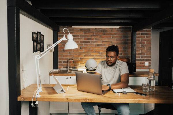 Man working on a laptop in a home office with exposed brick walls.